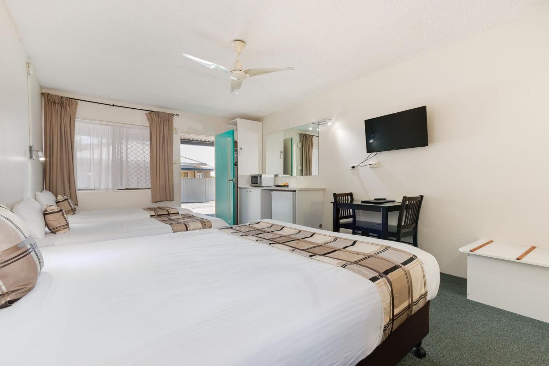 A hotel room with a large bed, a desk with a chair, a television mounted on the wall, and a ceiling fan.