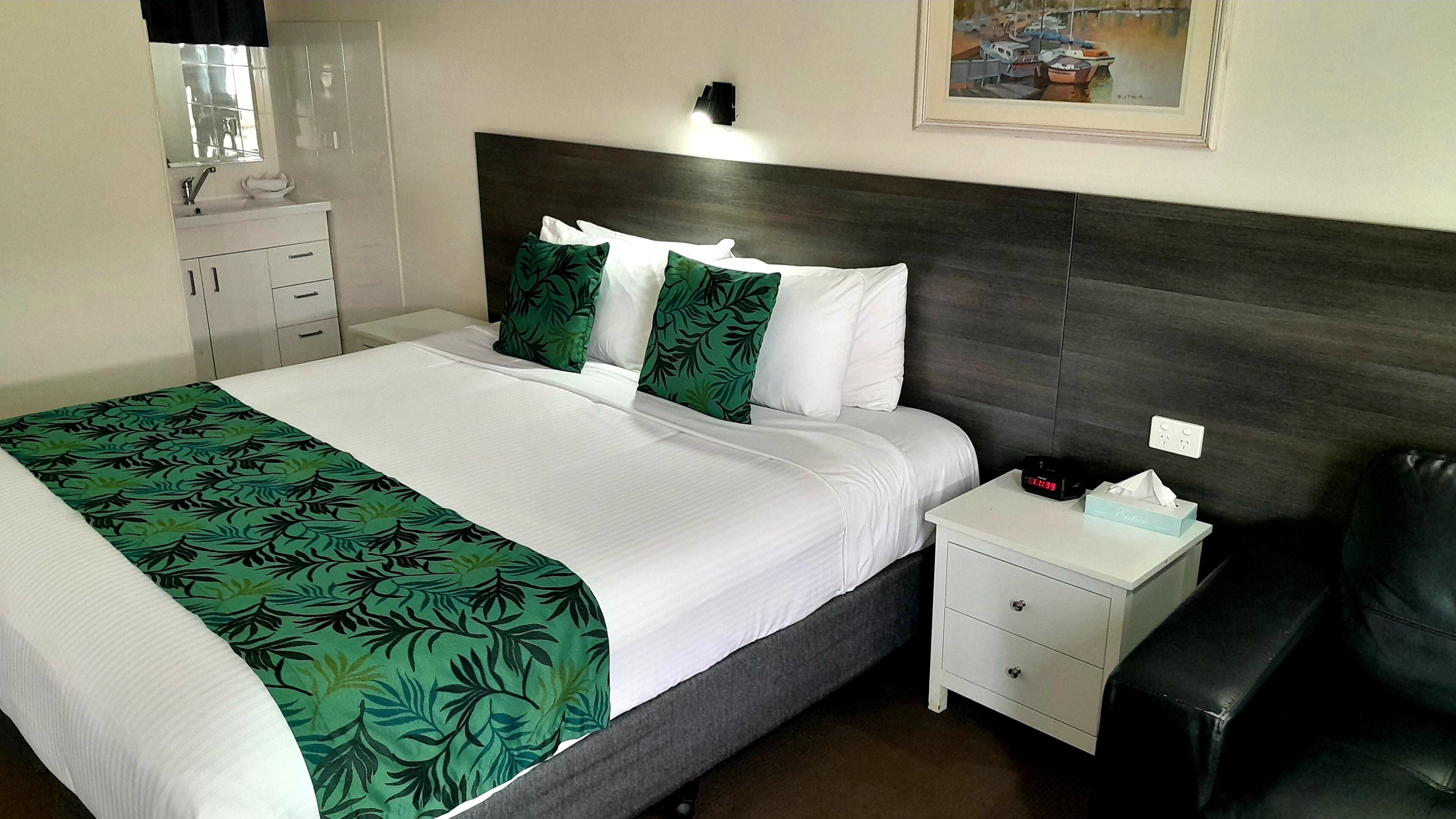 Habitación de hotel con cama, mesita de noche, un sillón de cuero negro, un cuadro en la pared y ventana con vista a barcos.