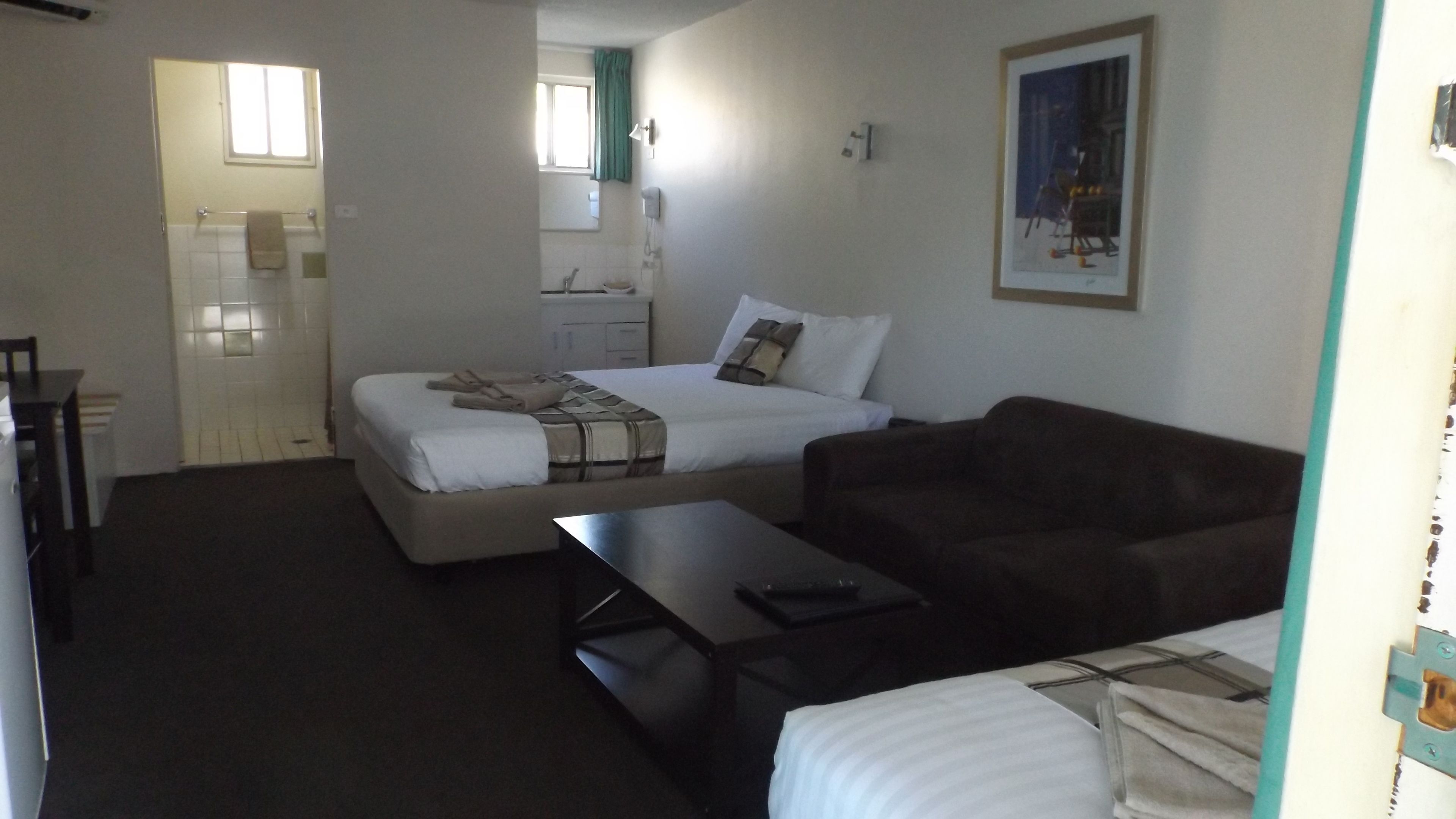 A bedroom with a bed, a sofa, a desk, and a bathroom visible in the background.