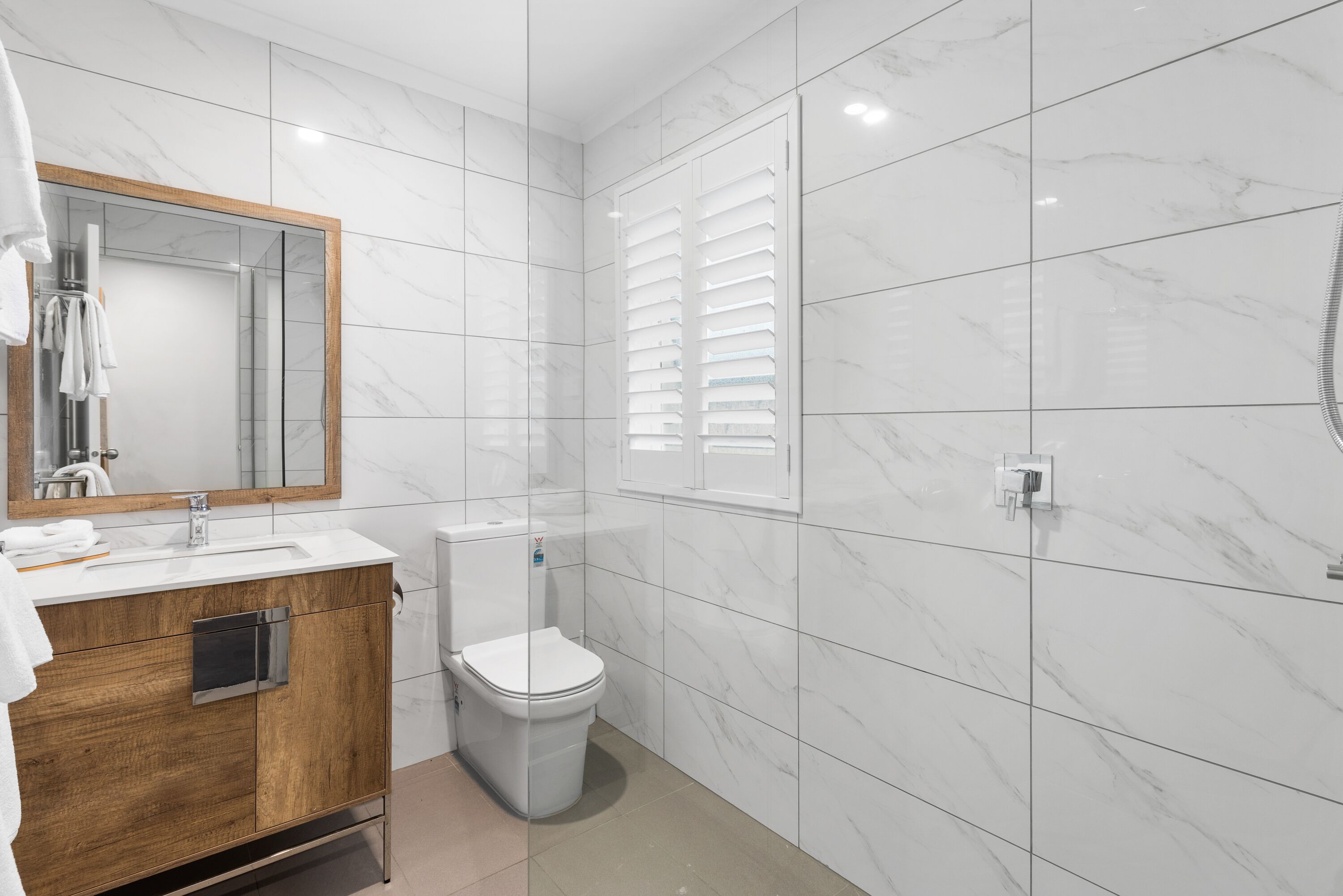 Une salle de bain moderne avec un sol en marbre, un meuble-lavabo en bois, des toilettes blanches et une cabine de douche en verre.