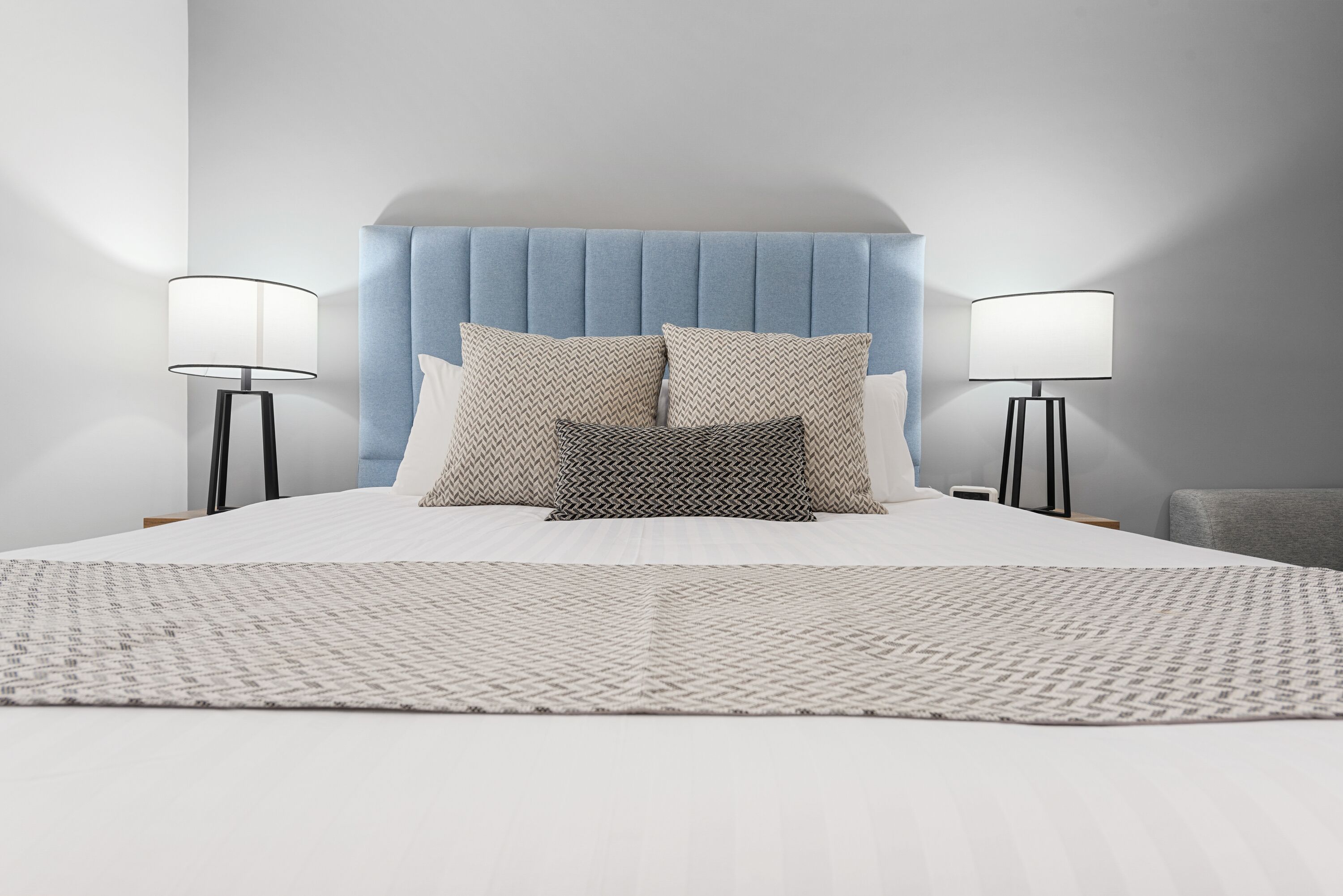 A neatly made bed with a patterned bedspread, a blue upholstered headboard, and two bedside lamps.
