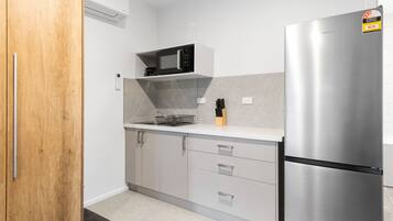 A modern kitchen with a stainless steel refrigerator, a microwave on a white shelf, and a wooden door.