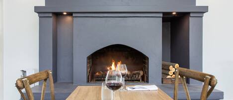 A dining table with two chairs, a fireplace, and a bottle of wine.