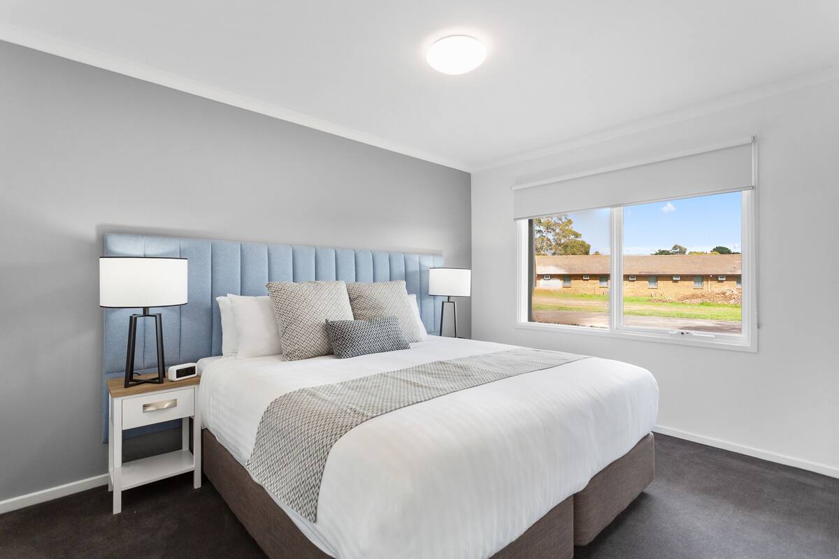 A modern bedroom with a large bed, two bedside tables, and a window with a view of the outside.
