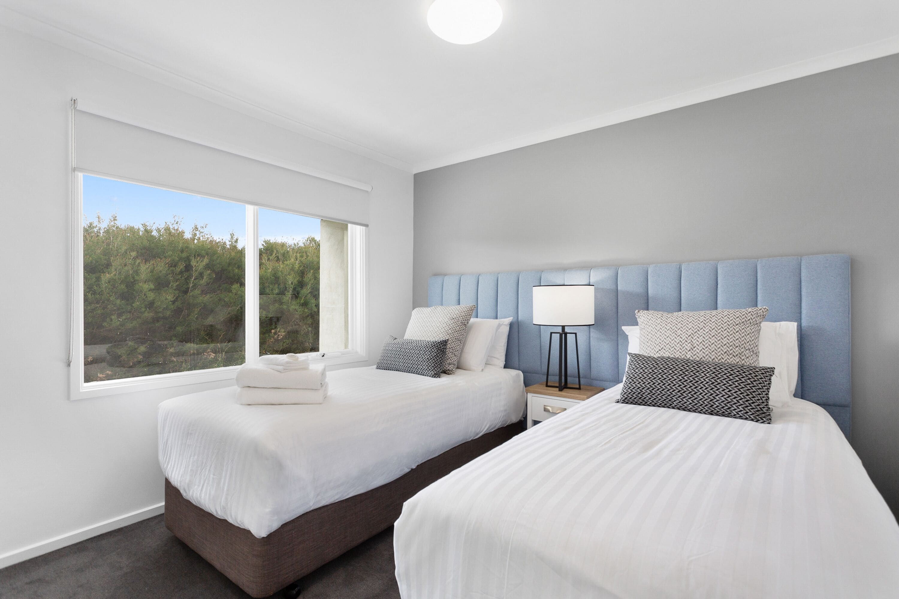A hotel room with two beds, a large window, and a view of trees.