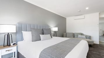 Ett modernt hotellrum med en stor säng, två sängbord, en grå soffa och ett litet bord med en lampa.