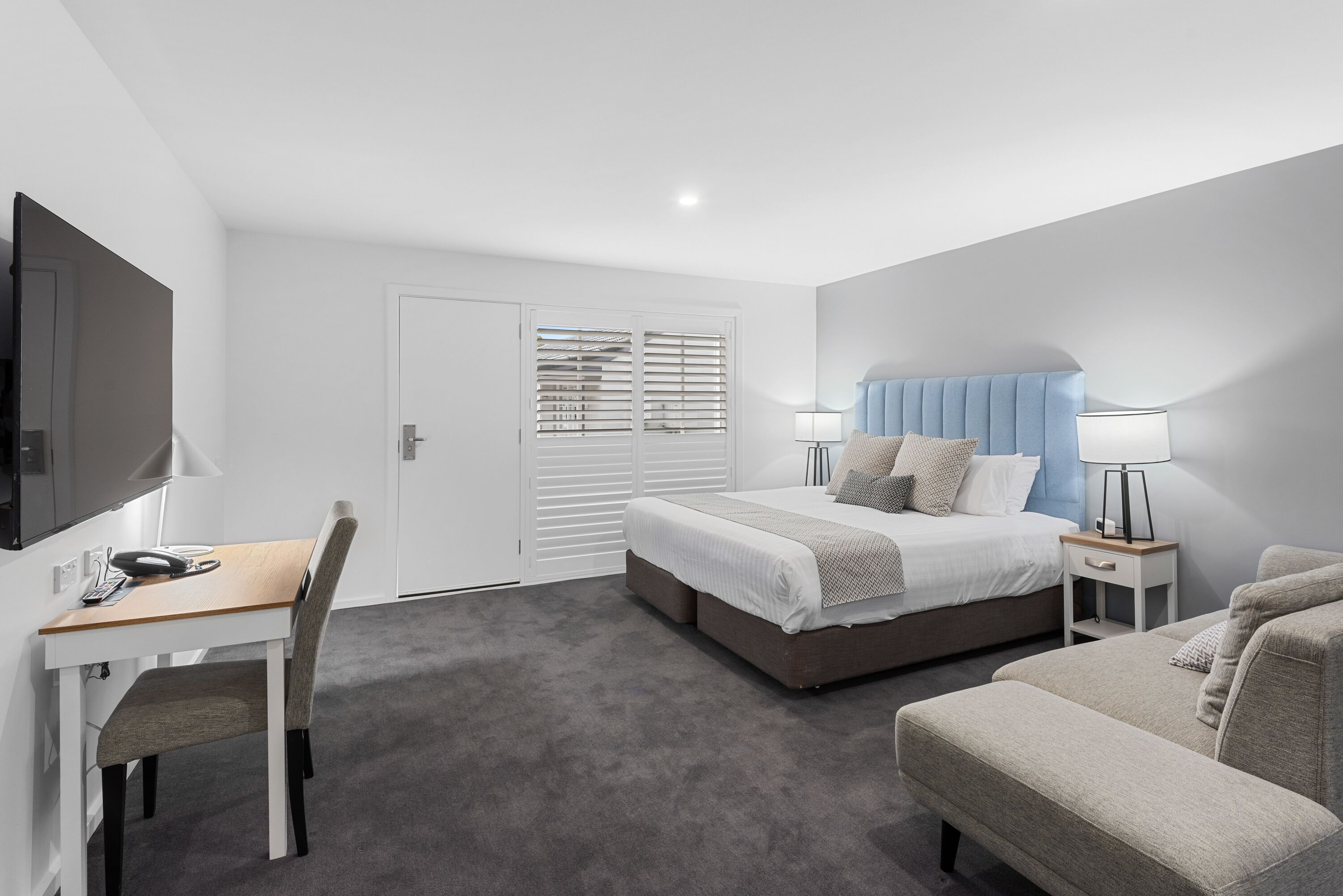 A modern bedroom with a bed, bedside tables, a desk, and a TV.