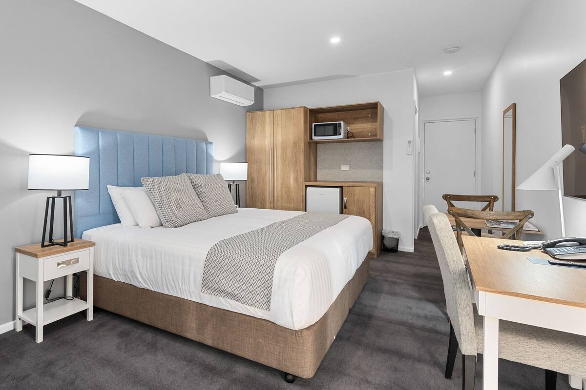 A modern bedroom with a large bed, bedside tables, a desk, and a microwave.