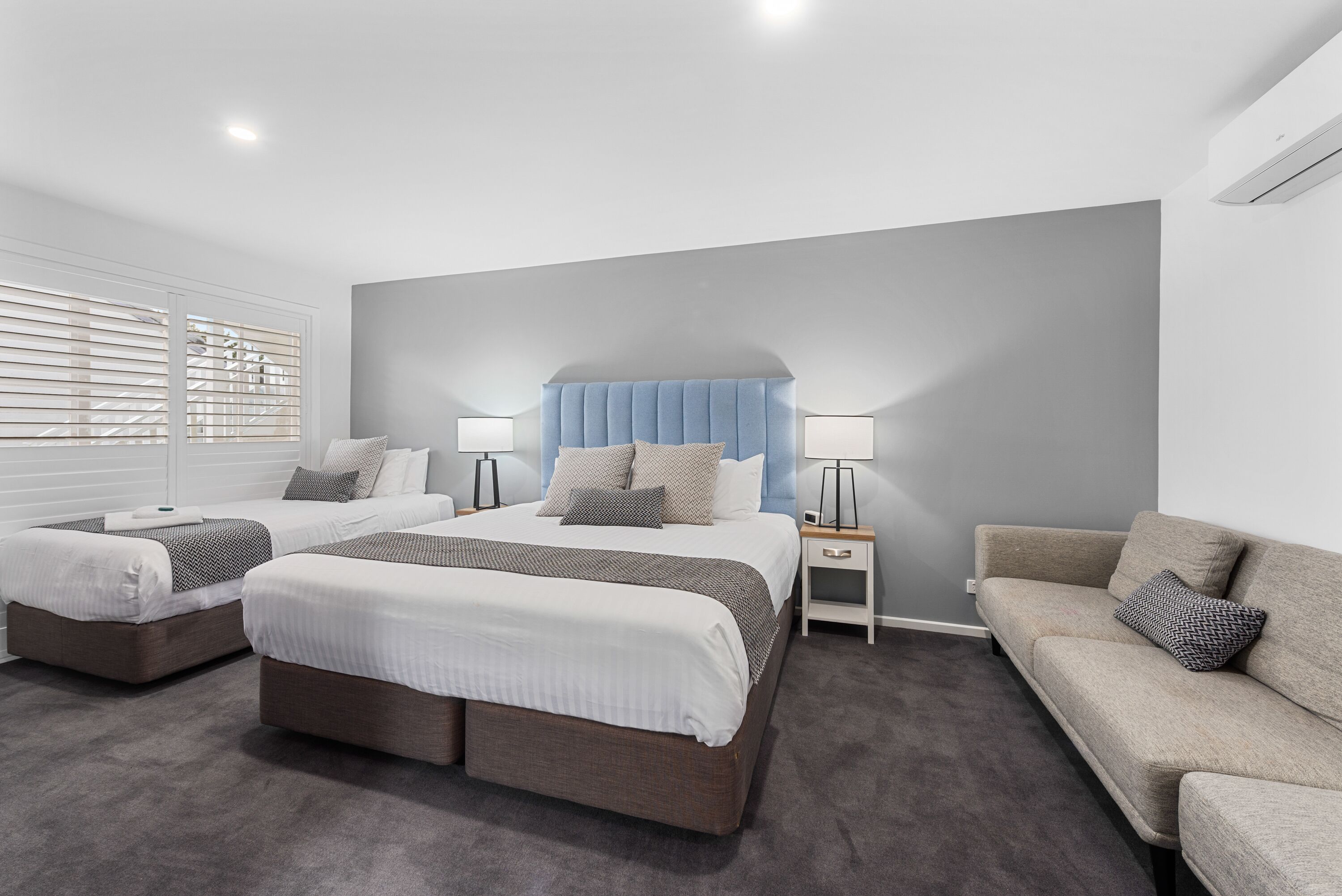 Un dormitorio moderno con dos camas individuales, una cama doble, un sofá y lámparas de noche.