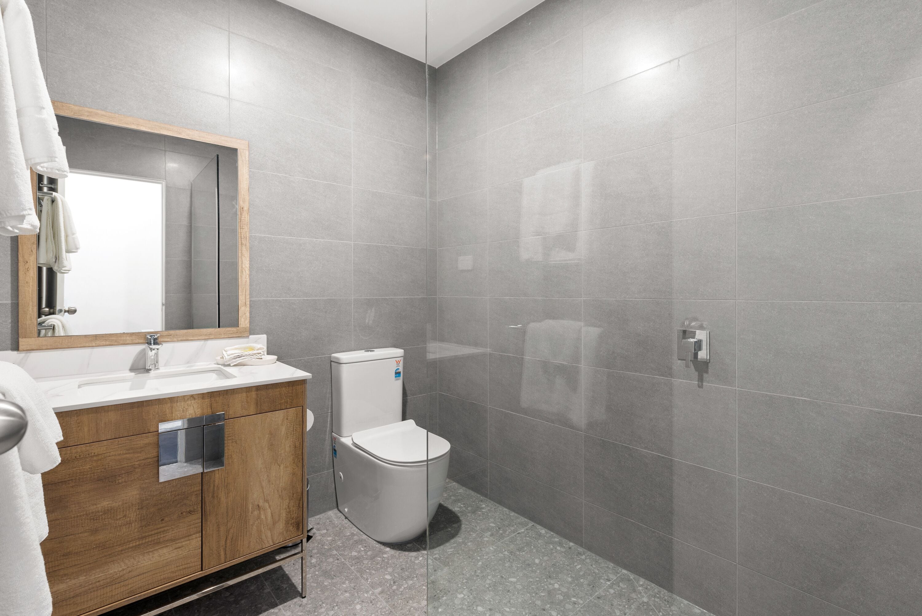 A modern bathroom with a wooden vanity, a white toilet, and a large mirror.