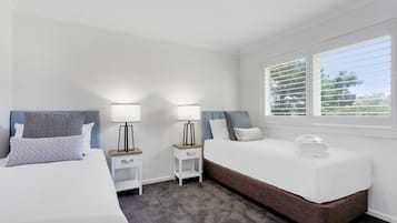 Une chambre avec deux lits, une fenêtre avec des stores et un sol recouvert de moquette.