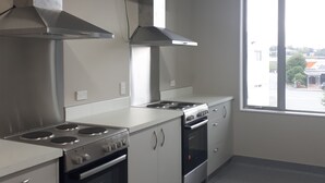 A modern kitchen with stainless steel appliances, white cabinetry, and a large window providing a view of the outside. - Northpark Motel (Timaru)