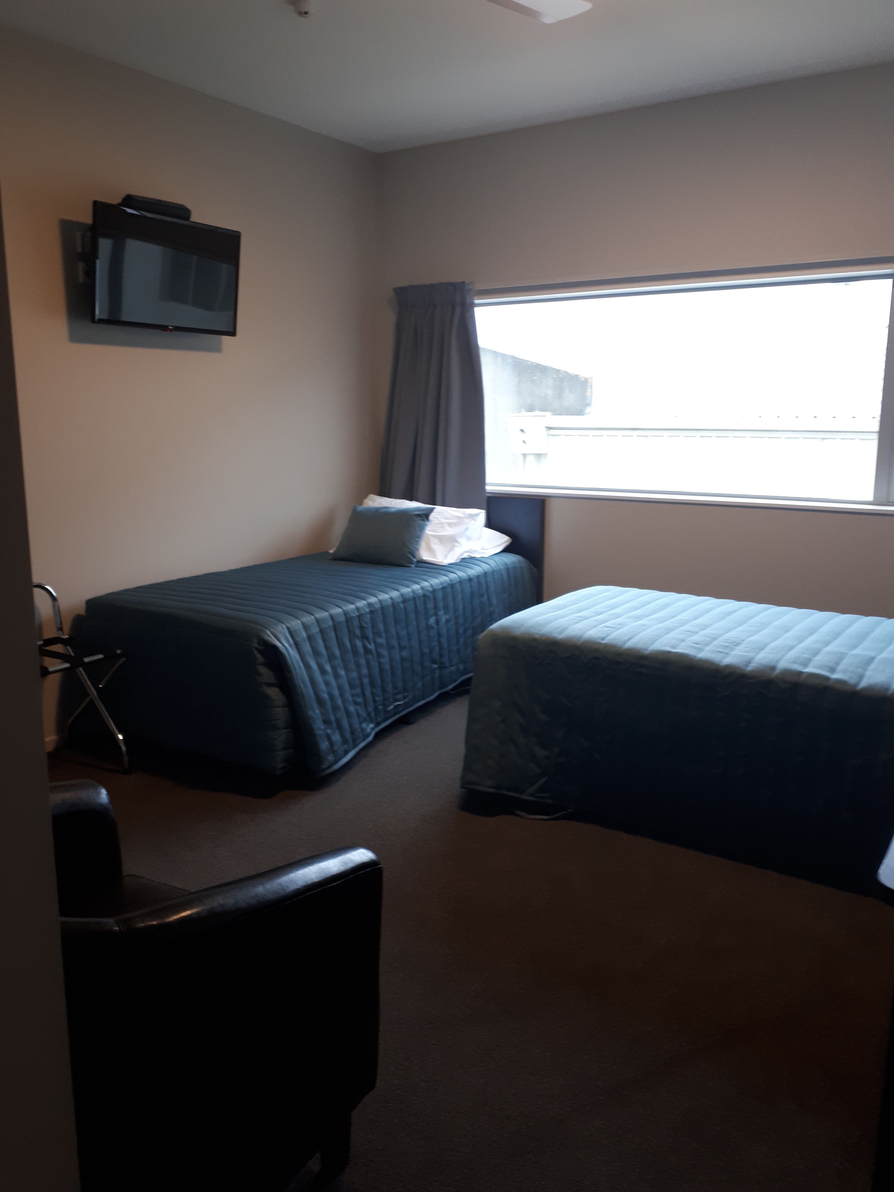 A hotel room with two single beds, a TV mounted on the wall, a window with curtains, and a chair.