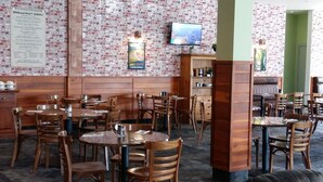 A restaurant with brick-patterned walls, wooden tables and chairs, a black leather couch, and a television mounted on the wall. - Northpark Motel (Timaru)