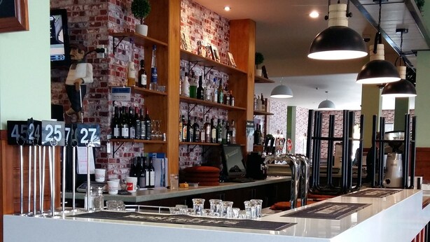 A modern bar area with a central counter, shelves with bottles, and hanging pendant lights. - Northpark Motel (Timaru)
