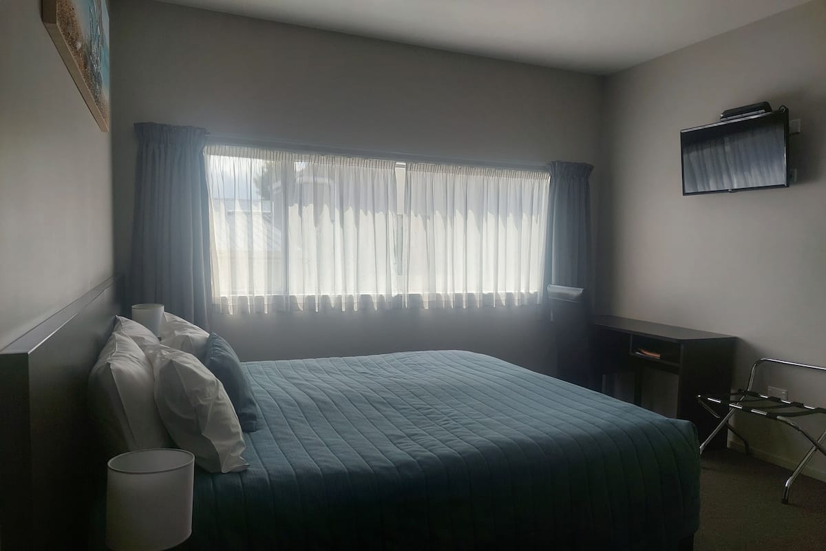 A hotel room with a bed, a desk, a chair, and a television mounted on the wall.