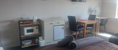 A hotel room with a bed, a desk, a microwave, a refrigerator, a chair, and a wall-mounted TV.