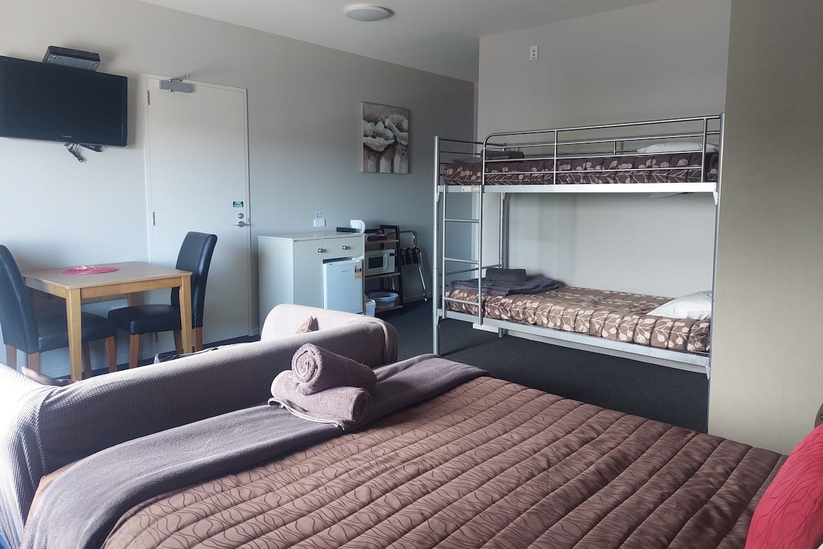 A room with a bunk bed, a desk with a chair, a small refrigerator, and a television mounted on the wall.