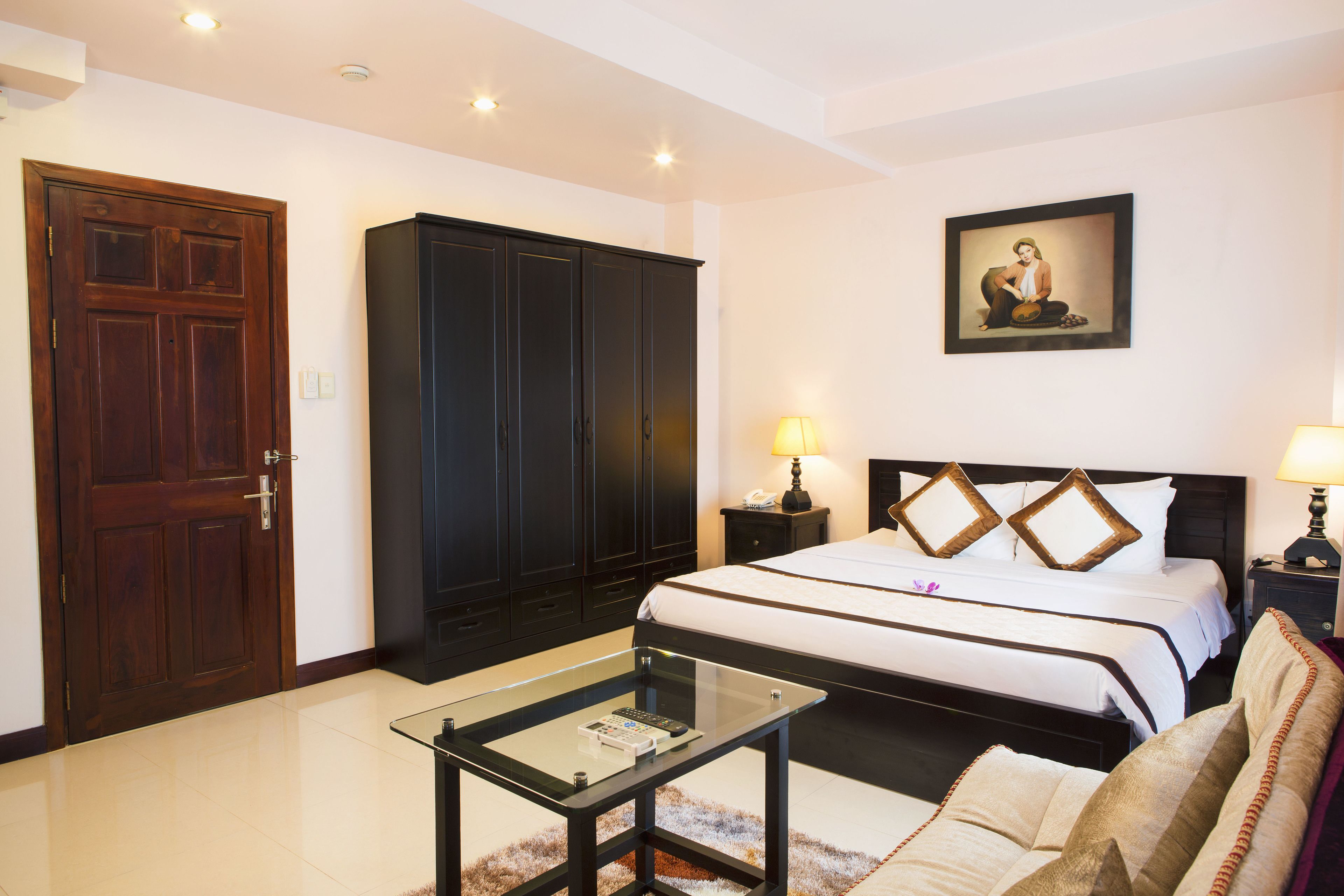 A hotel room with a large bed, a wardrobe, a glass coffee table, and two bedside lamps.
