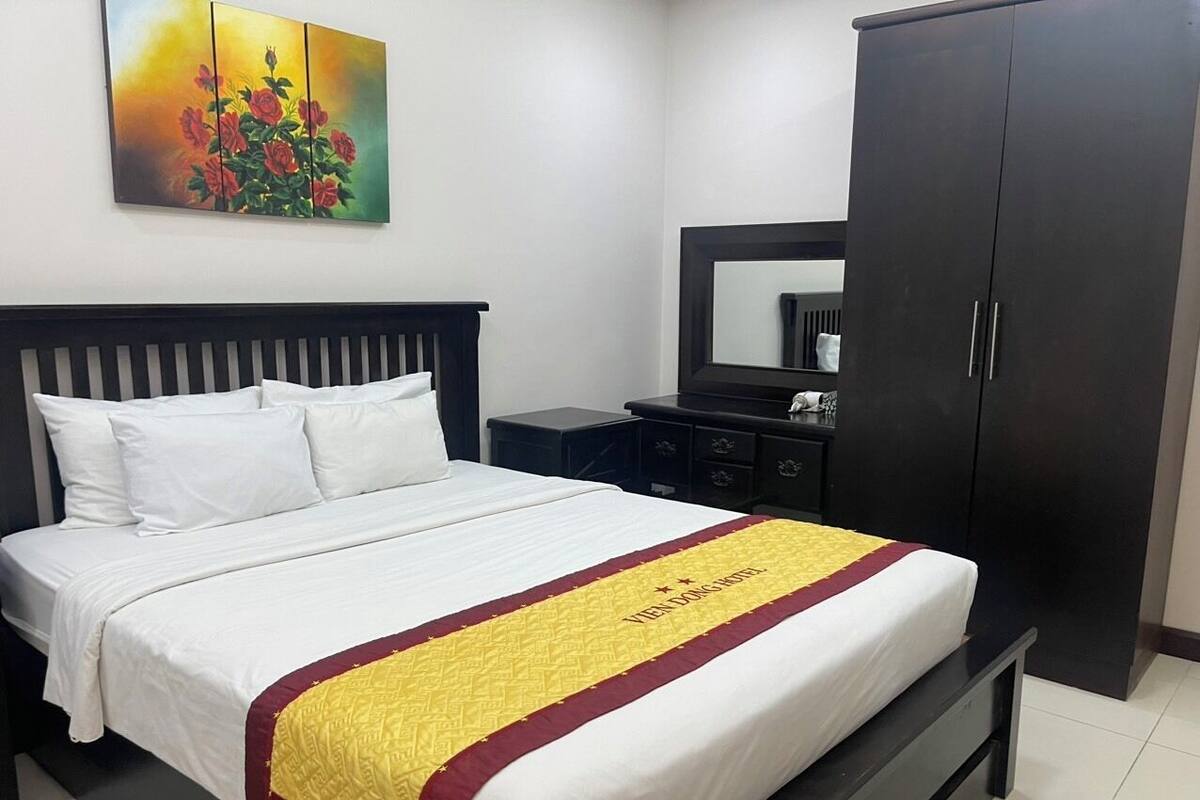 A hotel room with a bed, a nightstand, a wardrobe, and a painting on the wall.