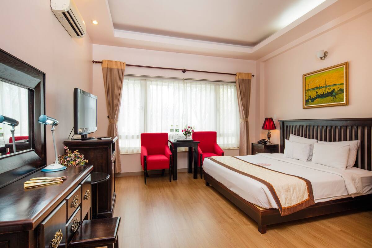 A hotel room with a bed, a desk with a computer, a chair, a TV, and a window with curtains.