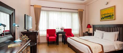 A hotel room with a bed, a desk with a computer, a chair, a TV, and a window with curtains.