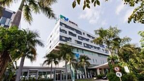 A modern hospital building with a clear entrance, palm trees, and a speed limit sign.