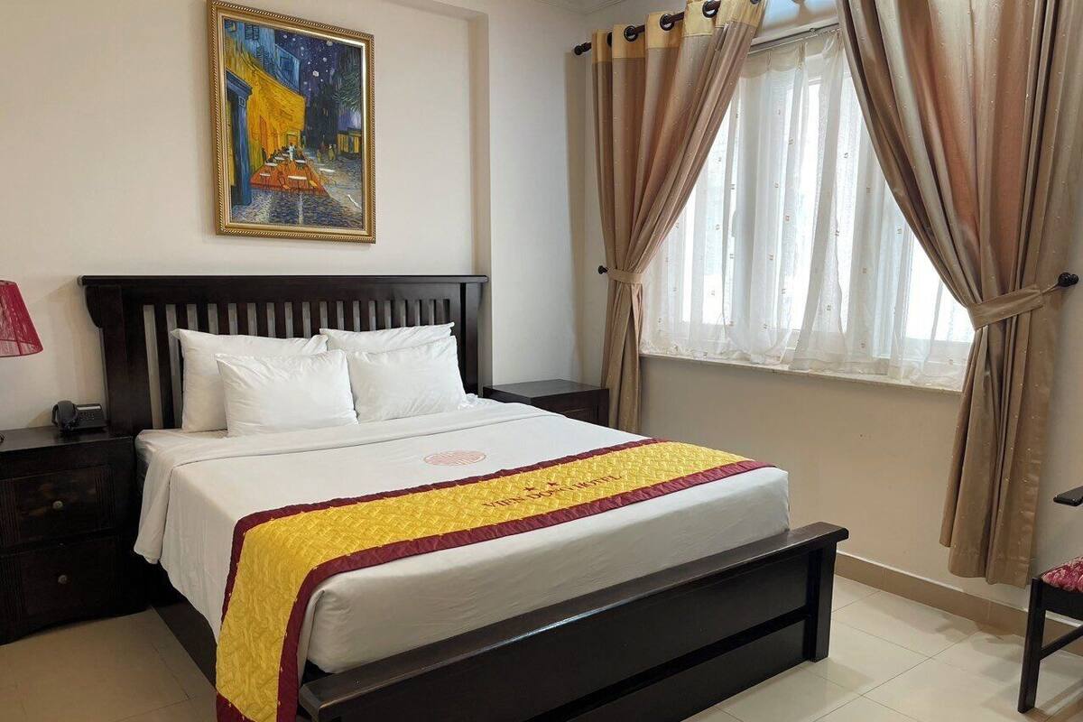 A neatly made bed with a white and yellow bedspread, a dark wooden headboard, and a painting above it.