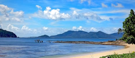 Una playa con aguas cristalinas, una orilla arenosa y montañas a lo lejos.