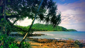 A beach with rocky shore, palm trees, and a forested hill in the background. - Mission Reef Resort (Wongaling Beach)