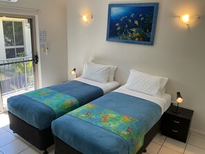 Una habitación de hotel con dos camas, cada una con una colcha azul y almohadas blancas. Hay un cuadro de peces en la pared sobre las camas.