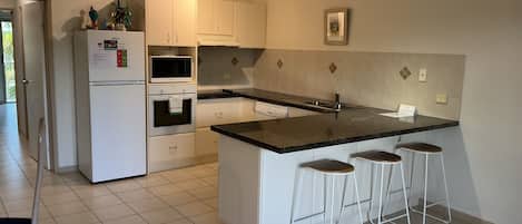 A modern kitchen with white cabinetry, a black countertop, and a built-in island with bar stools.