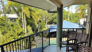 A covered outdoor seating area with a table and chairs, surrounded by a railing, overlooking a pool and lush greenery. - Mission Reef Resort (Wongaling Beach)