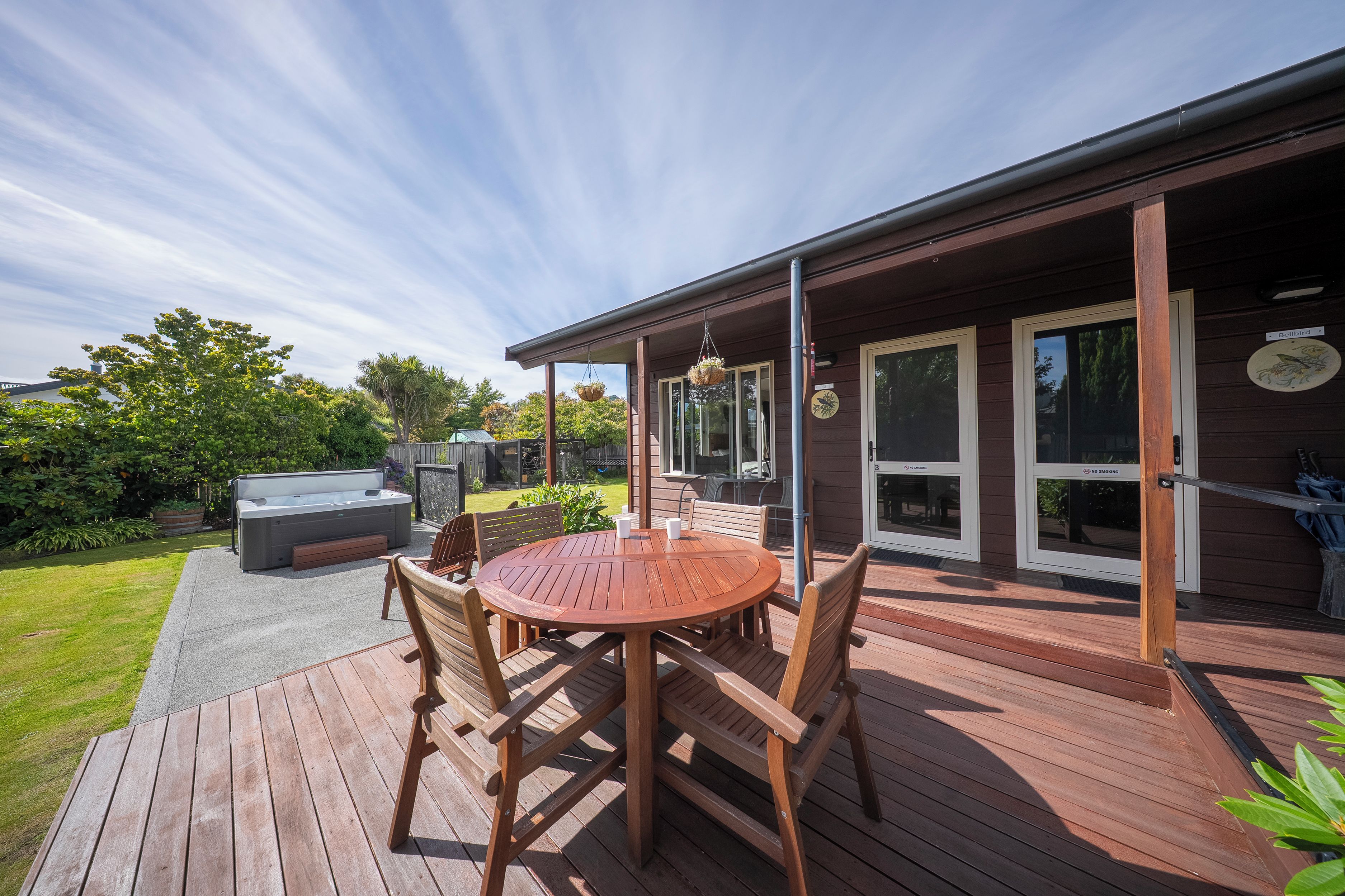 Una terraza de madera con una mesa redonda y sillas, un jacuzzi y un porche cubierto con una parrilla.