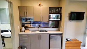 Eine kompakte Küche mit integriertem Mikrowellenherd, Spüle und kleinem Kühlschrank. Es gibt einen Holzschrank und ein Regal mit Weingläsern.
