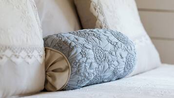 A bed with white and patterned pillows, a beige throw, and a lamp in the background.