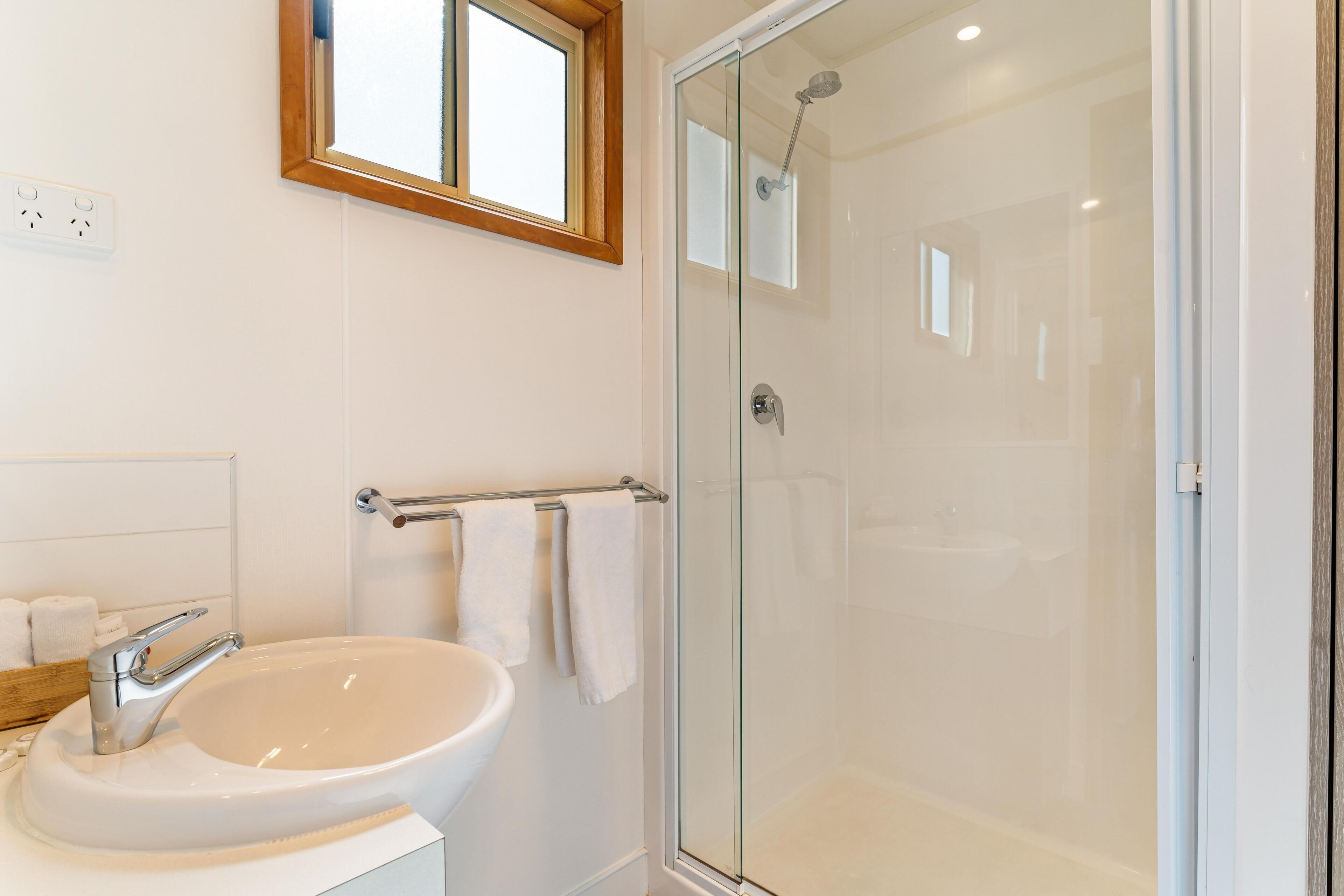 Un bany amb dutxa de vidre, un lavabo blanc i una barra de tovalloles.