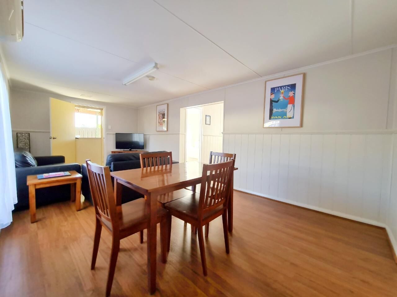 Un coin repas avec une table et des chaises en bois, un canapé et un téléviseur en arrière-plan.