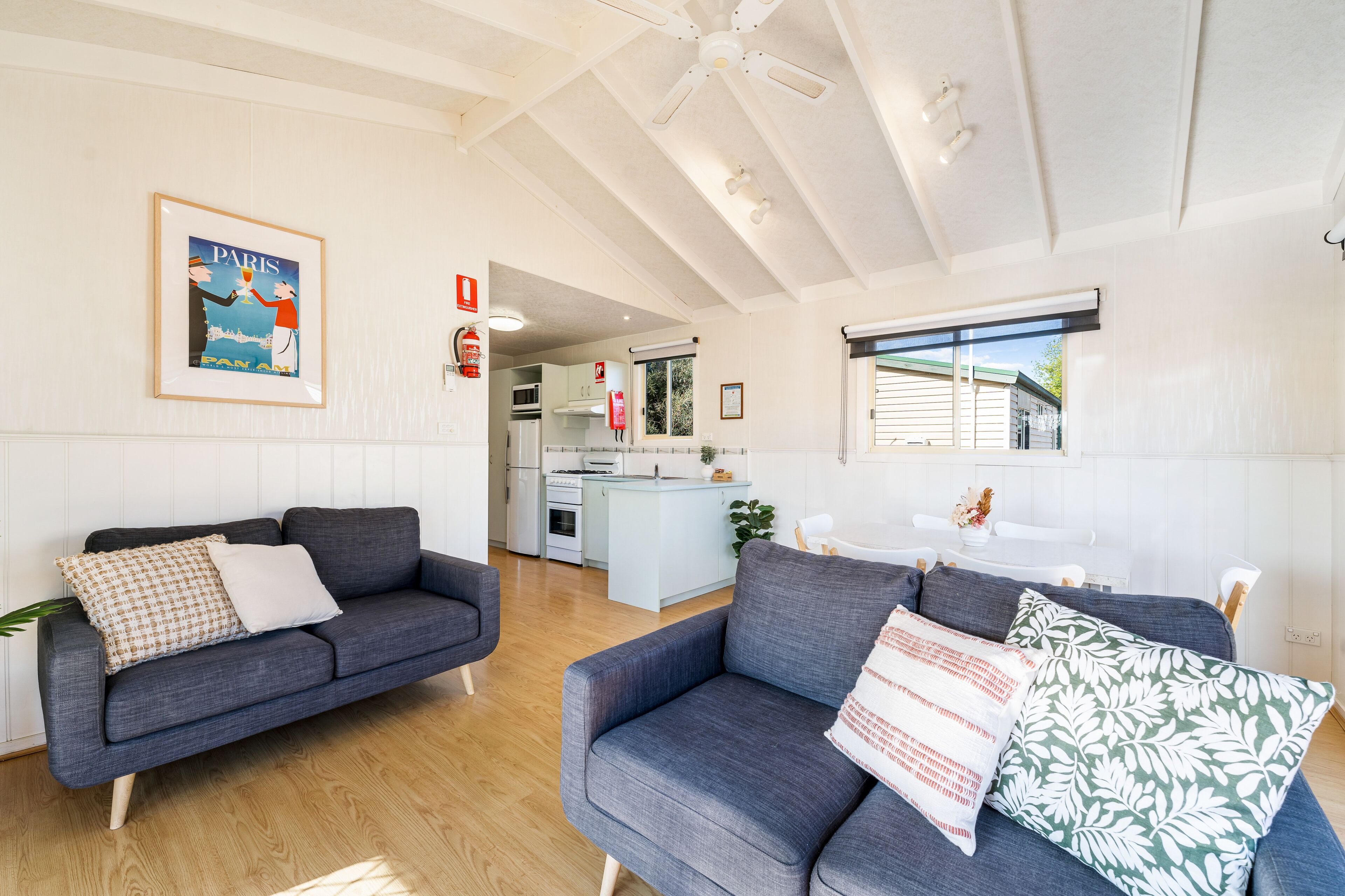 Ein modernes Wohnzimmer mit zwei grauen Sofas, Holzboden, Deckenventilator und einer Küche im Hintergrund.