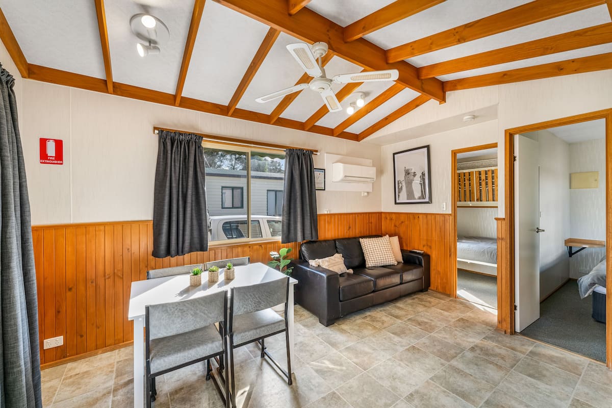 Ein Zimmer mit Holzboden, Deckenventilator, Esstisch mit Stühlen, einer Couch und einem Bett.