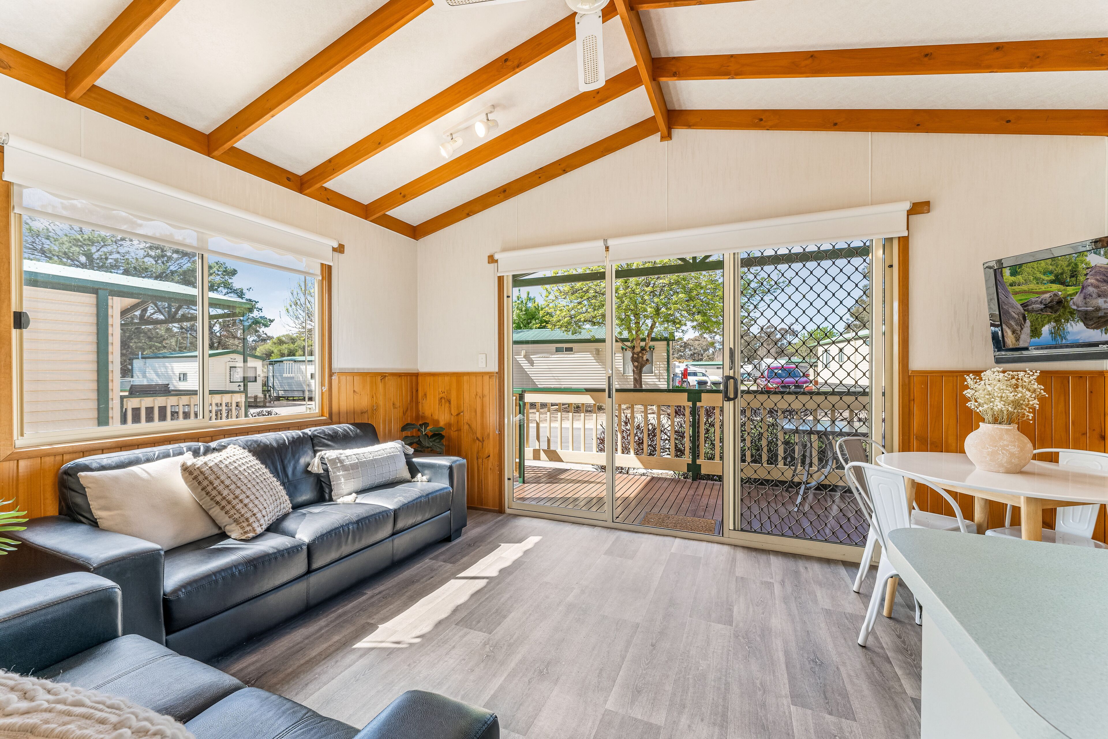 Un amplio salón con techo de madera, un sofá, una mesa de comedor y un ventanal corredero que da a una terraza exterior.