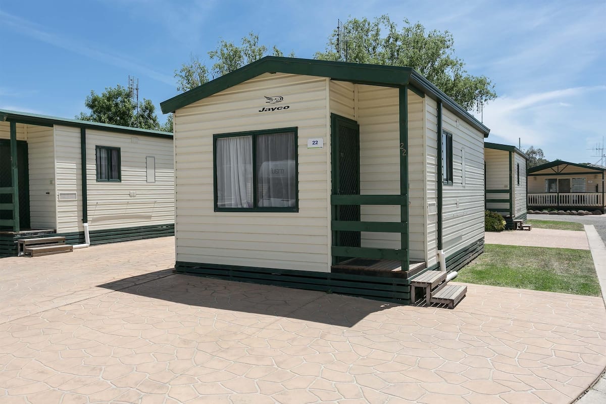 Ein Mobilheim mit grüner Dachhaut und Hinweisschild Nummer 22, gelegen in einem Caravanpark mit gepflasterten Wegen und weiteren ähnlichen Häusern im Hintergrund.