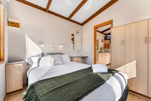 A bedroom with a bed, a wooden wardrobe, a bedside table, a mirror, and a small cabinet. - BIG4 Tasman Holiday Parks - Bendigo (White Hills)