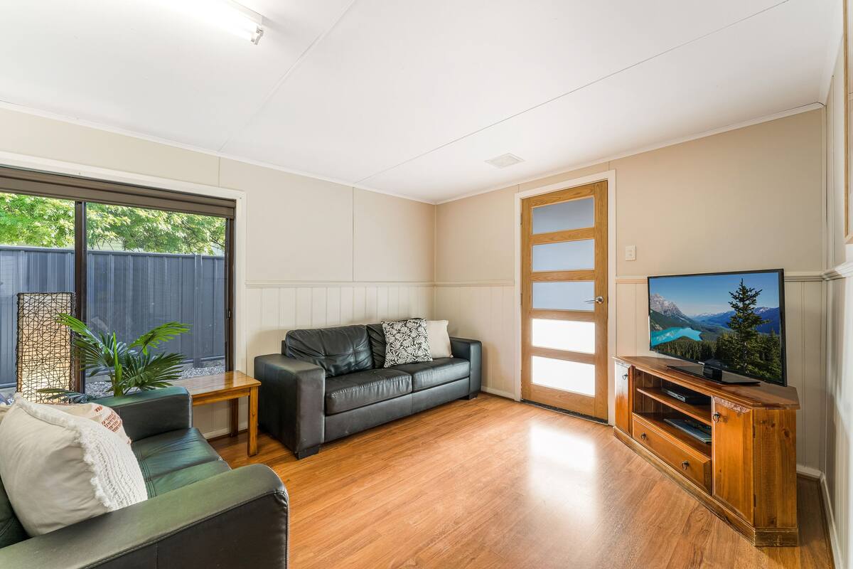 Ein Wohnzimmer mit einer Ledersofa, einer Holz-Unterhaltungseinrichtung und einem Fernseher, der eine Berglandschaft zeigt.