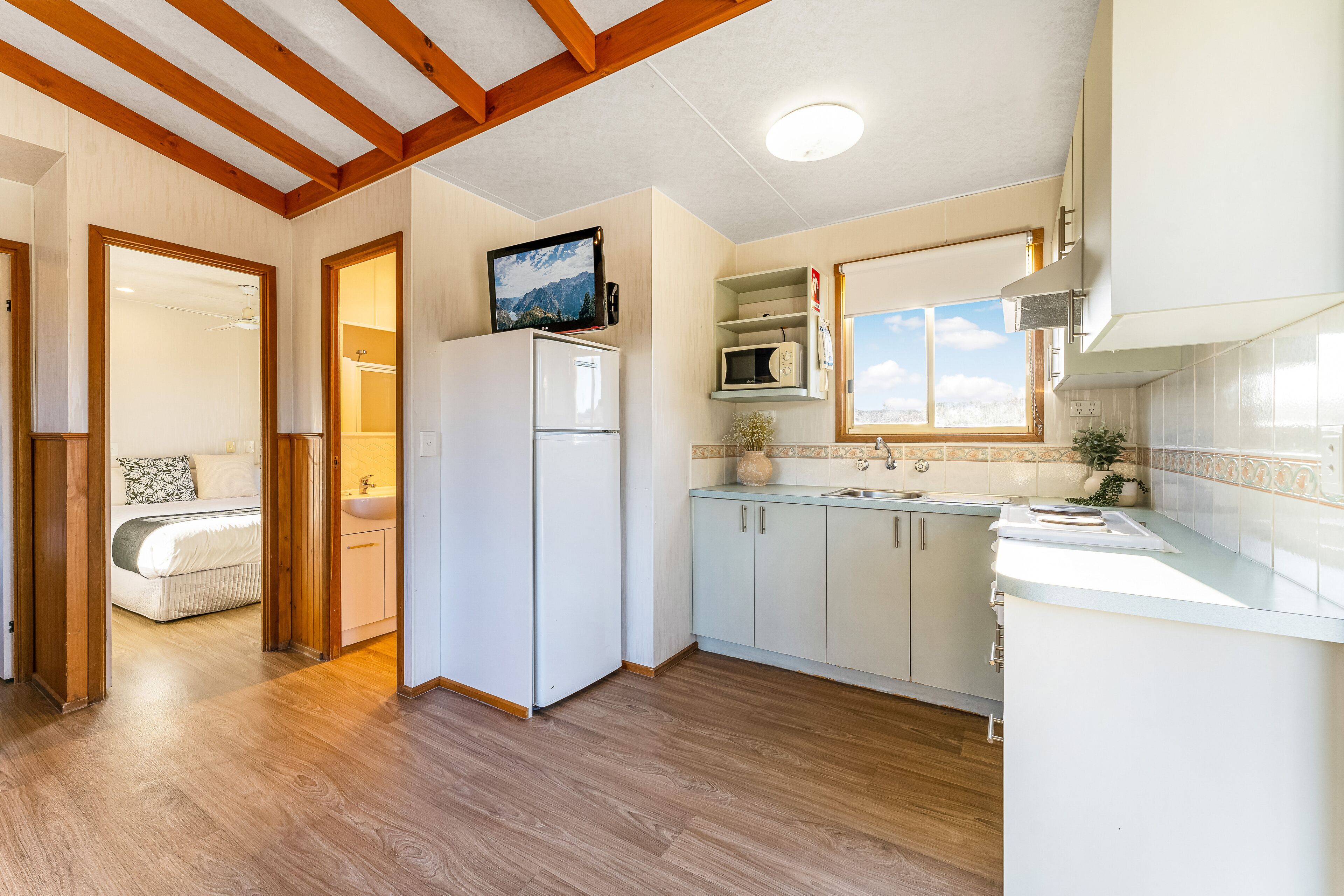 A modern kitchen with wooden flooring, white cabinets, a built-in microwave, and a large window.