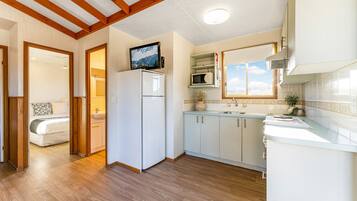 A modern kitchen with wooden flooring, white cabinets, a built-in microwave, and a large window.