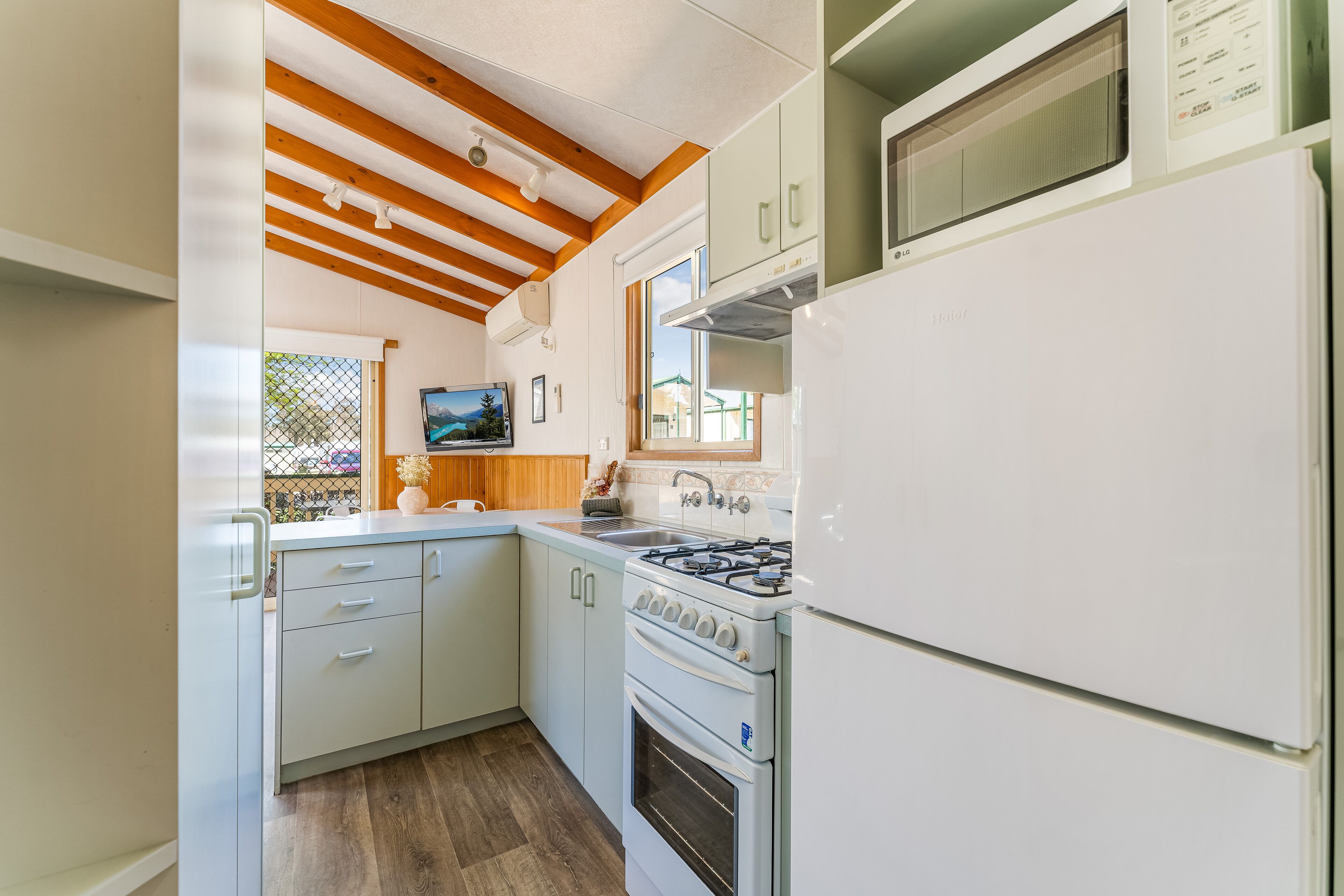 Una cocina compacta con armarios blancos, estufa a gas, microondas y refrigerador.