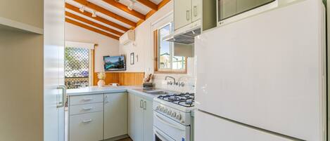 Una cocina compacta con armarios blancos, estufa a gas, microondas y refrigerador.