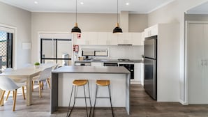 Cocina moderna con armarios blancos, refrigerador de acero inoxidable y una isla central con taburetes.