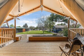 A covered outdoor deck with wooden flooring, a seating area with chairs, and a view of a grassy yard and buildings in the background. - BIG4 Tasman Holiday Parks - Bendigo (White Hills)